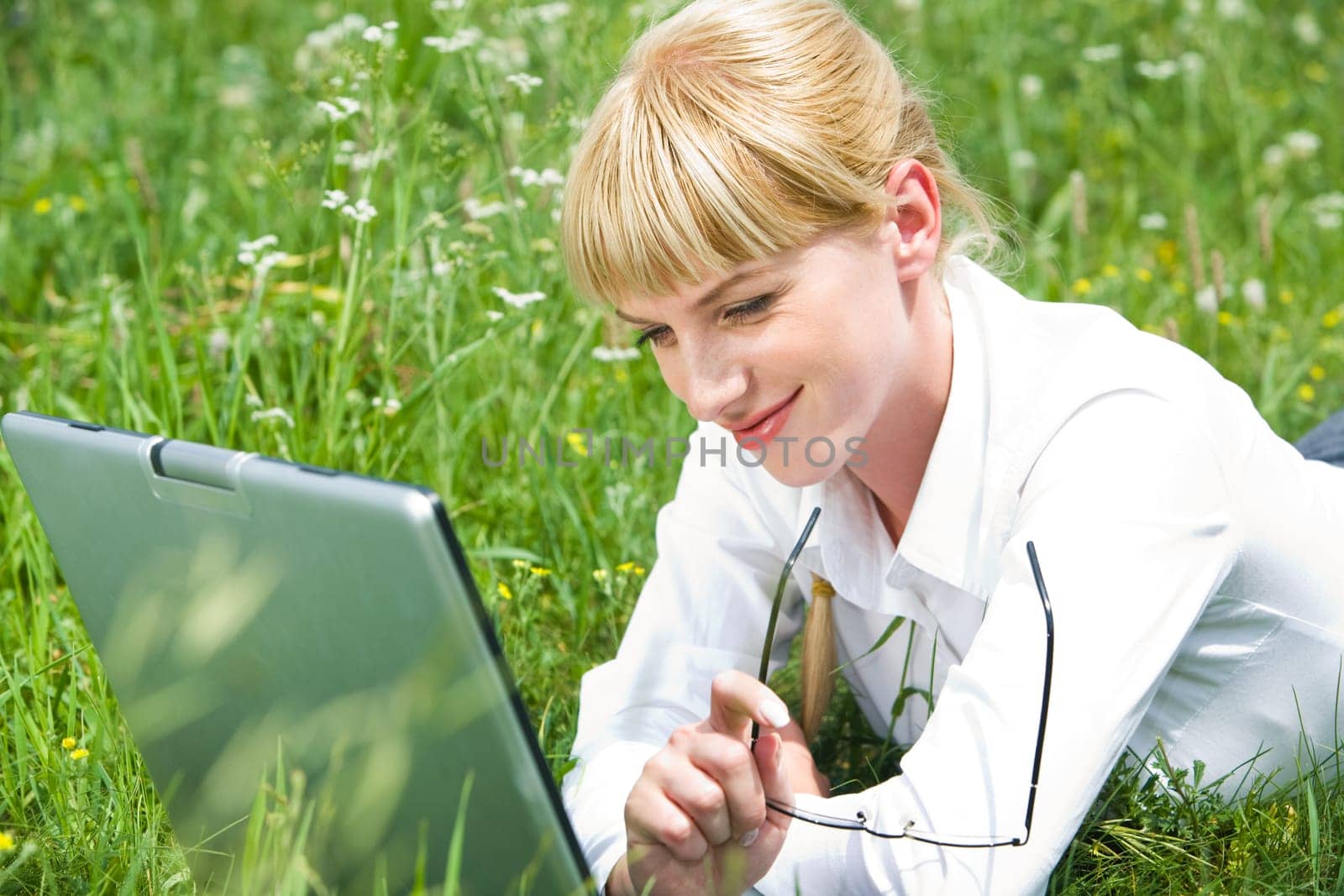 Image of businesswoman working on laptop while lying on green grass outside
