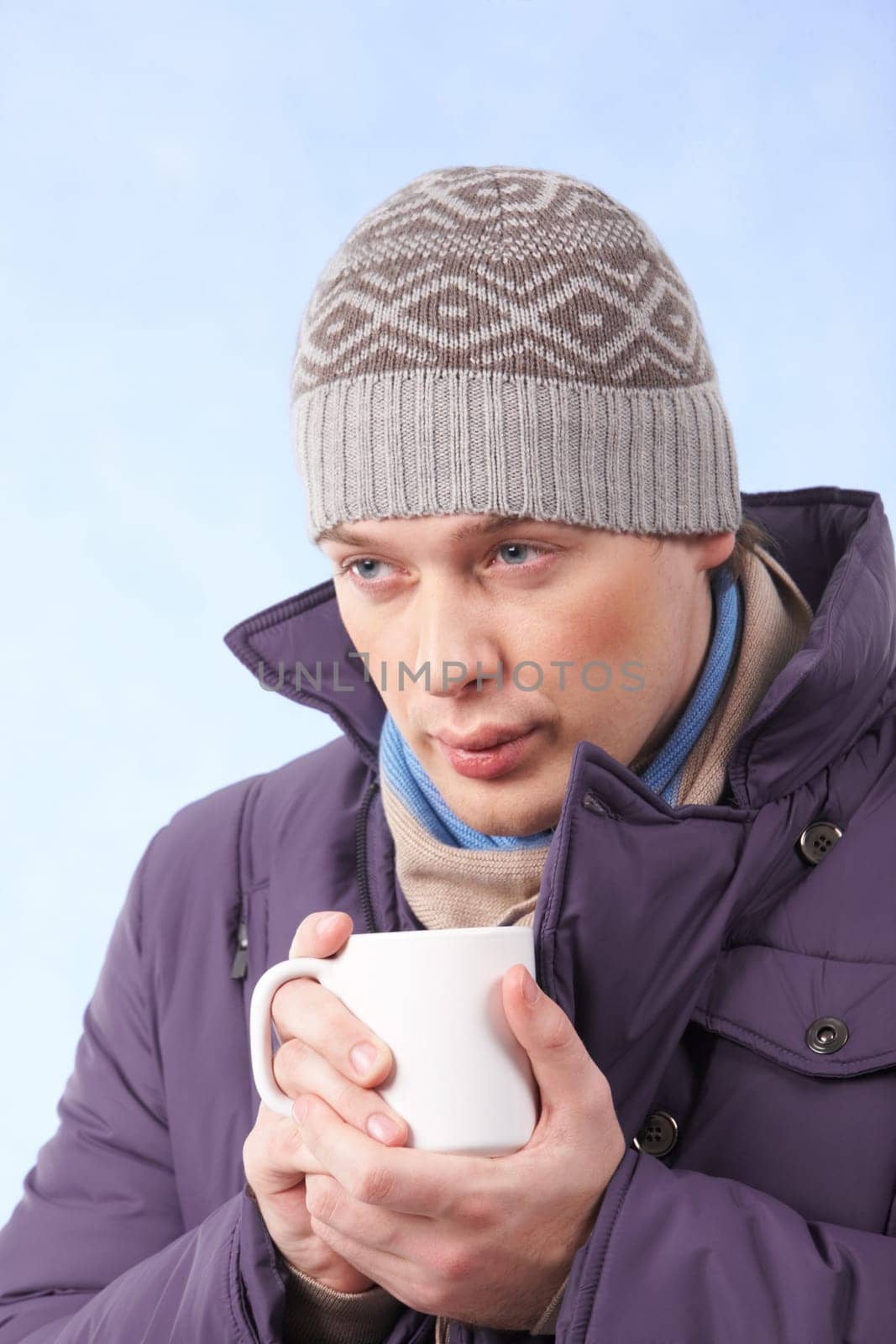 Portrait of young man in warm clothes drinking hot tea or coffee