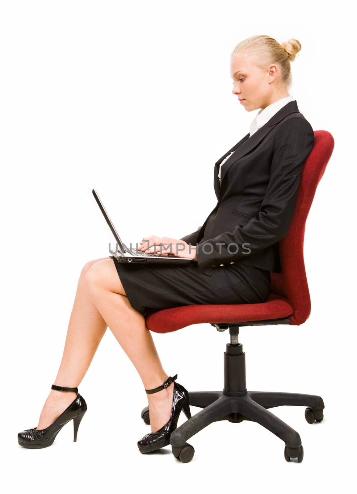 Profile of serious businesswoman sitting on arm-chair and typing on laptop