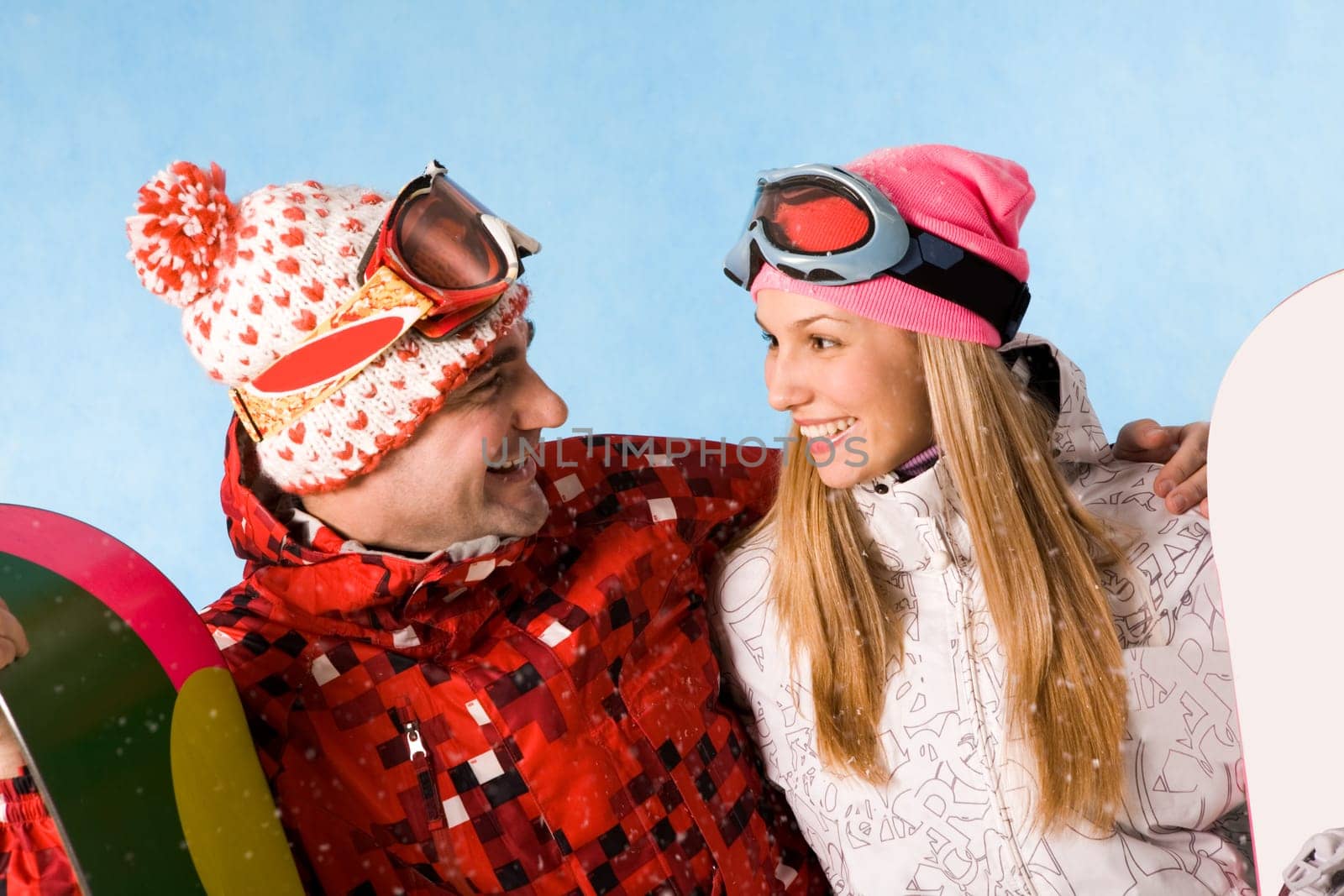 Portrait of happy couple with snowboards communicating in snowfall