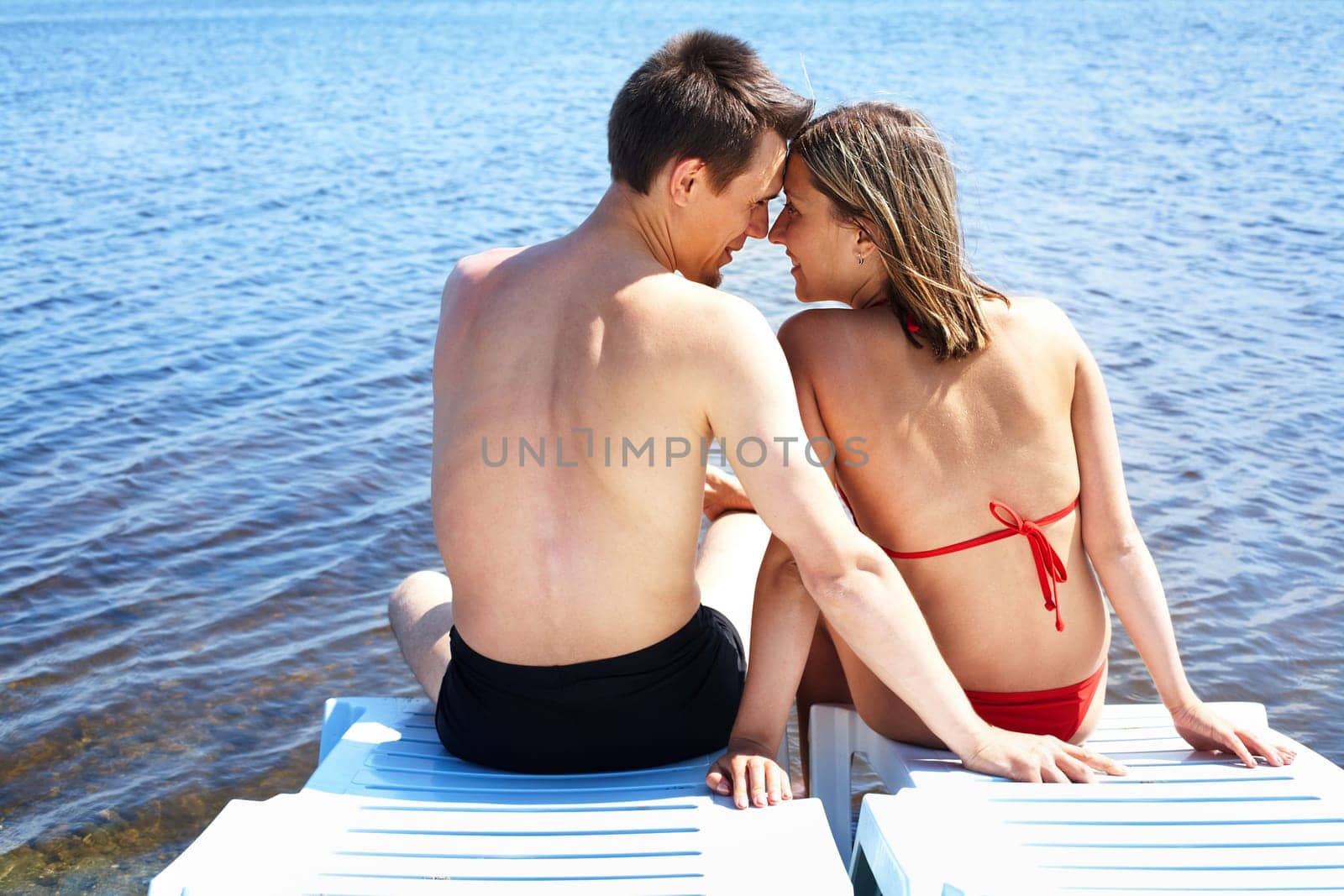 Back view of two people sitting on deck chairs and looking at one another on resort