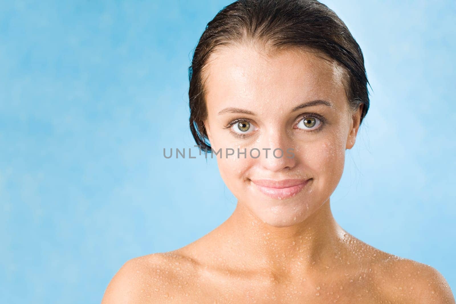 Portrait of pretty girl covered by waterdrops looking at camera over blue background