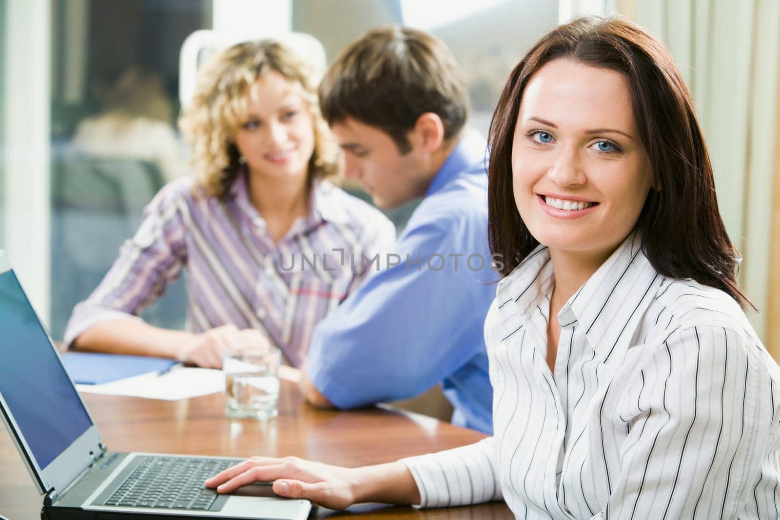 Young smart smiling woman sitting at the table and typing on her laptop