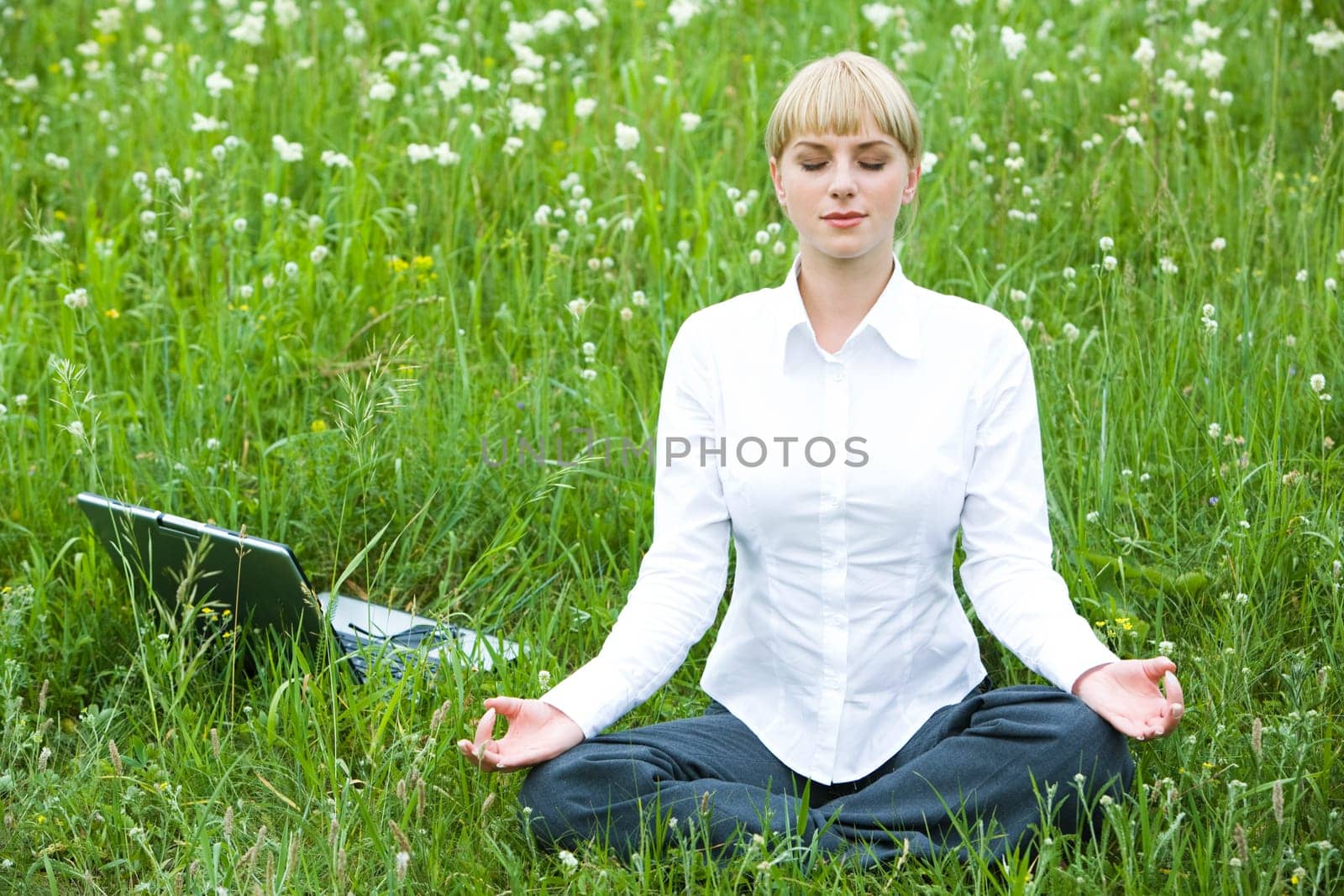 Portrait of meditating woman sitting on meadow in summer during break