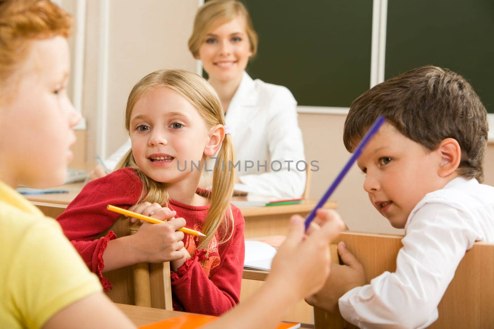 Portrait of schoolchildren sitting in classroom and speaking with their teacher behind