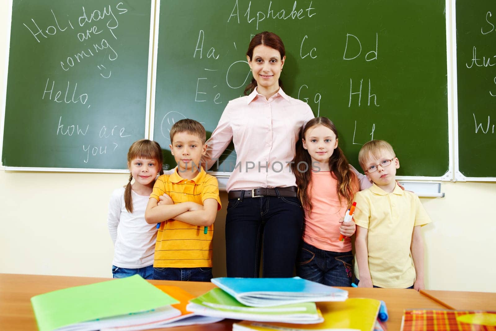 Line of cute schoolchildren looking at camera with their teacher in the middle
