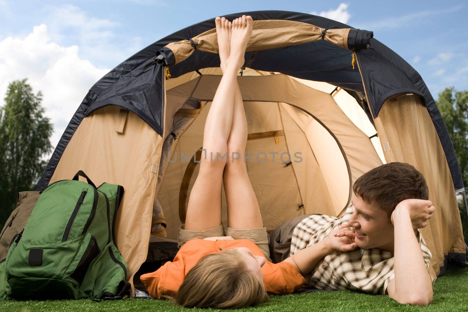 Pretty girl touching boyfriend while lying on grass near tent during summer vacations