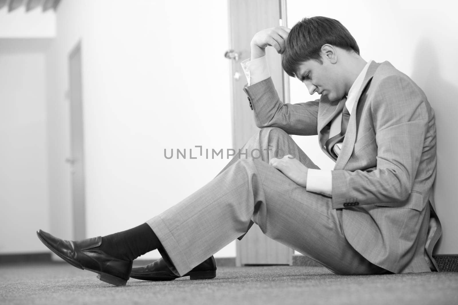 Black and white photo of thinking man sitting on the floor against wall
