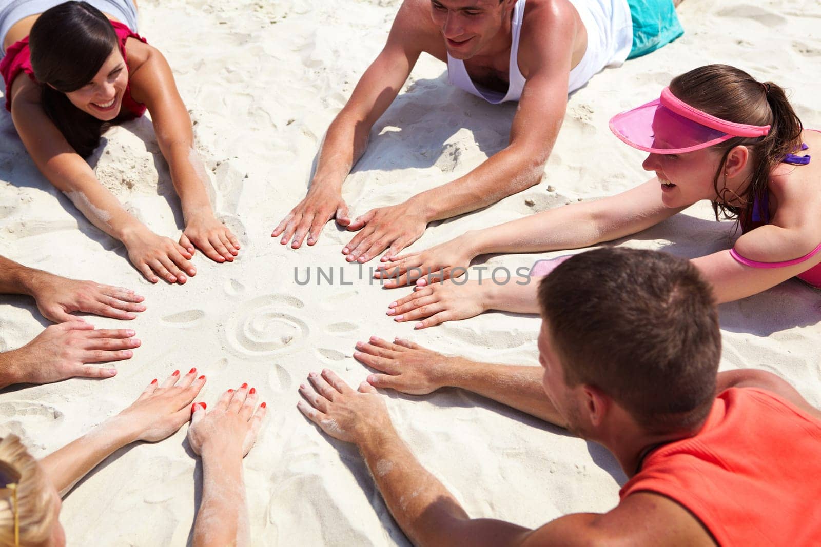 Image of several teens lying on beach and keeping their hands on sand in the form of circle