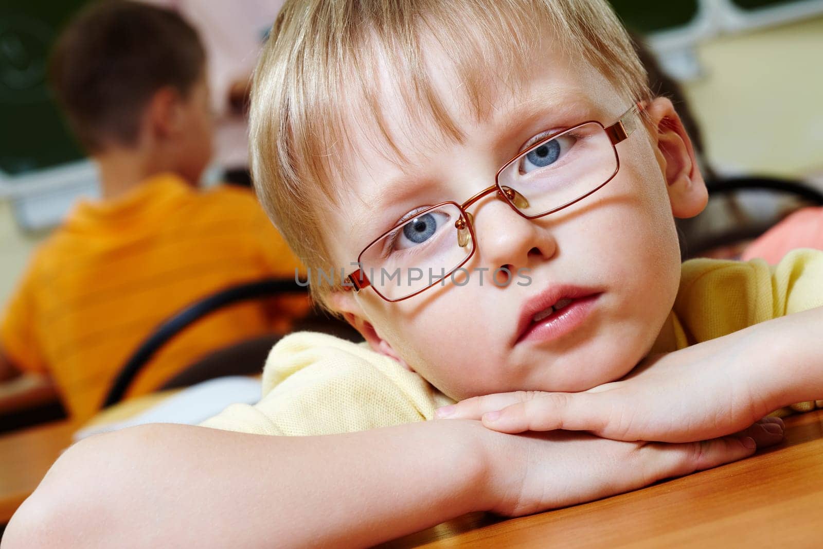 Close-up of schoolboy putting his head on arms and looking at camera