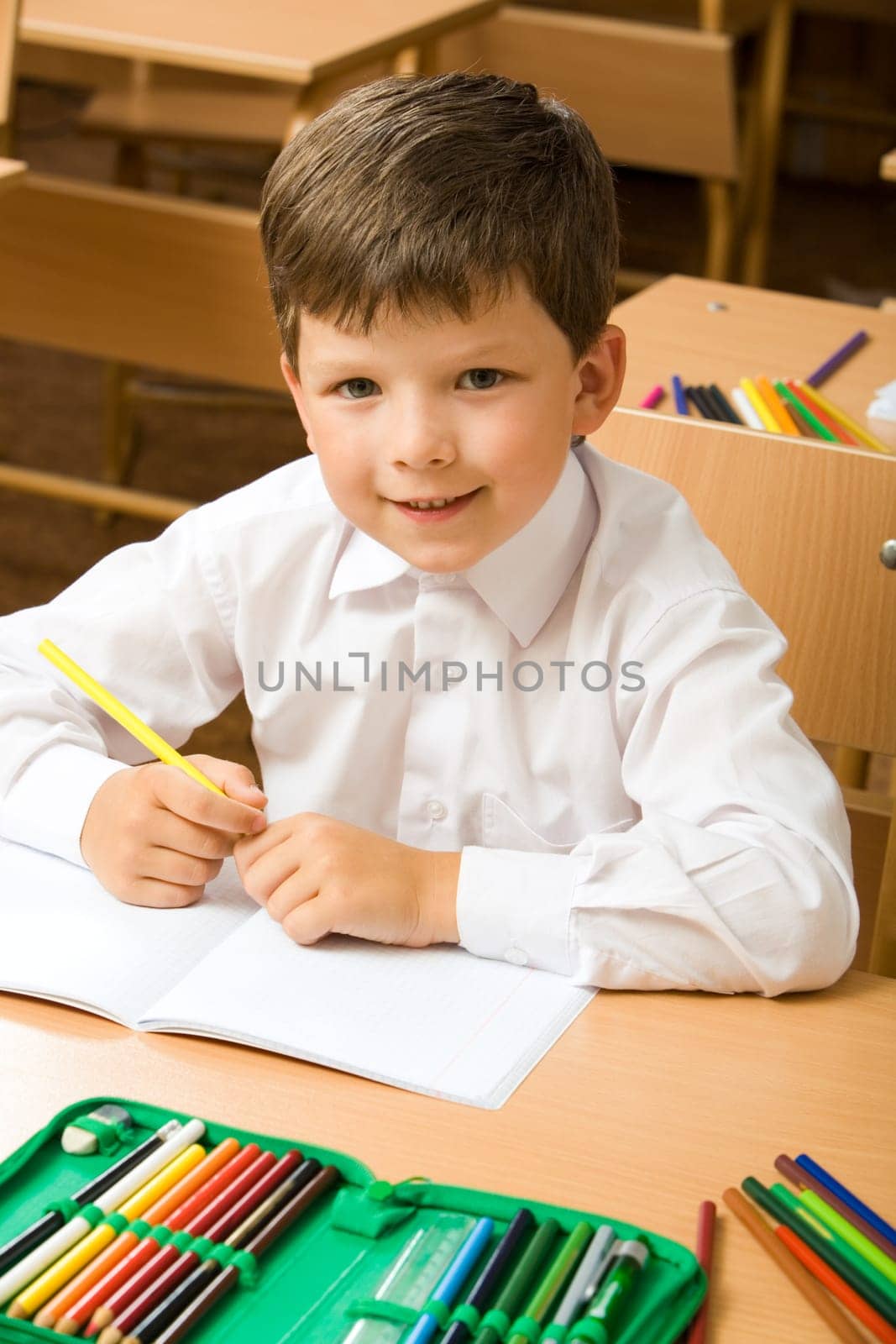 Portrait of cute boy sitting at desk with copybook and colored pencils near by