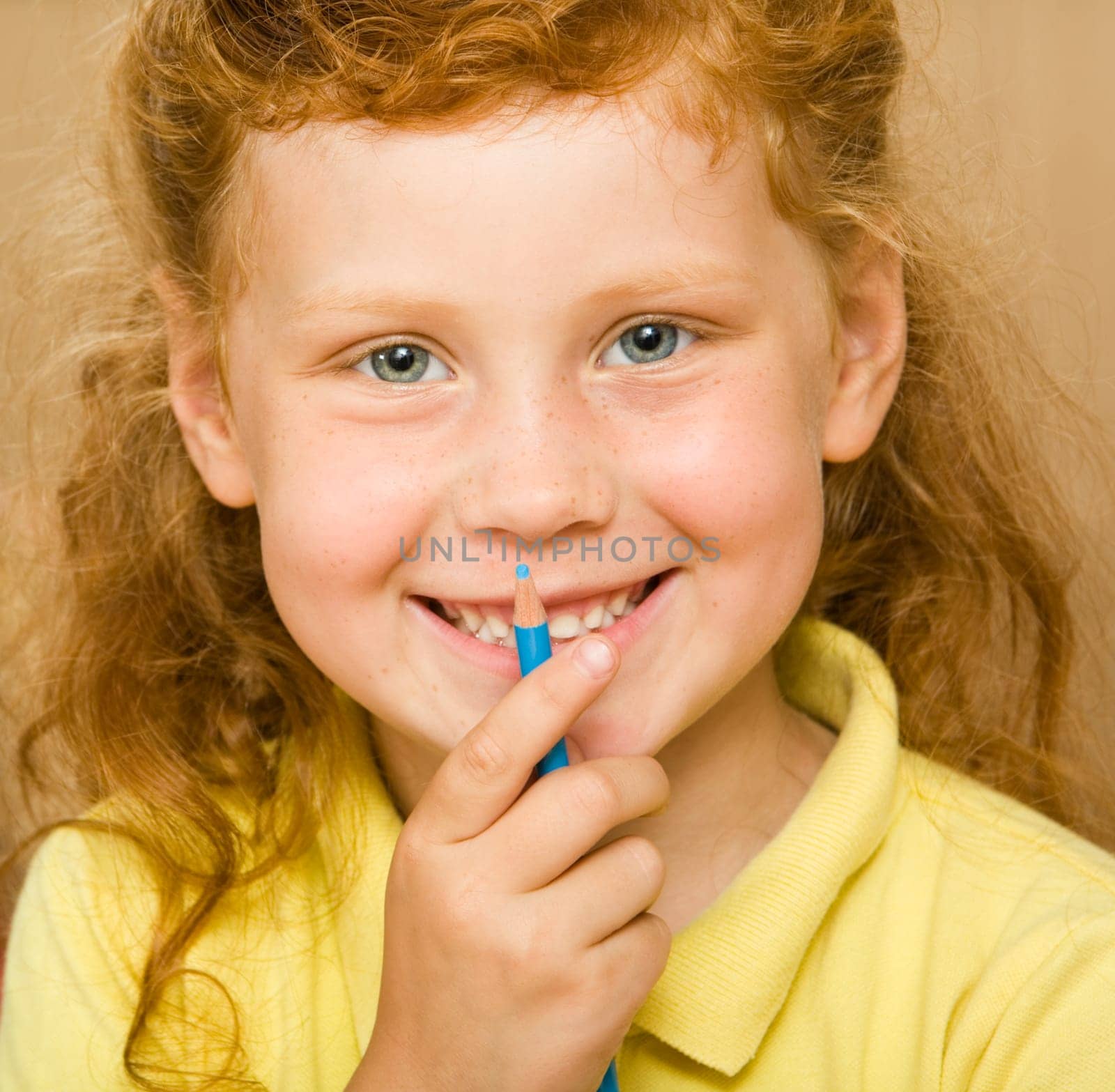 Face of red-headed girl holding blue pencil by her mouth looking at camera with smile