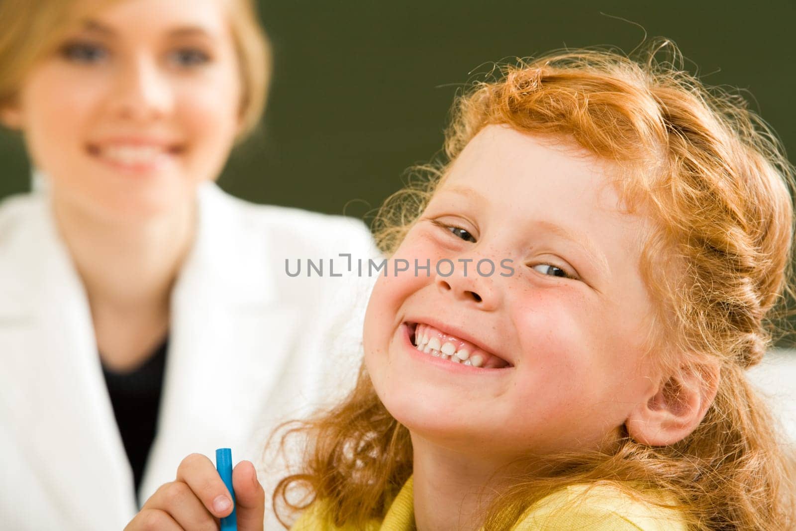 Close-up of happy girl laughing while looking at camera on background of smart teacher