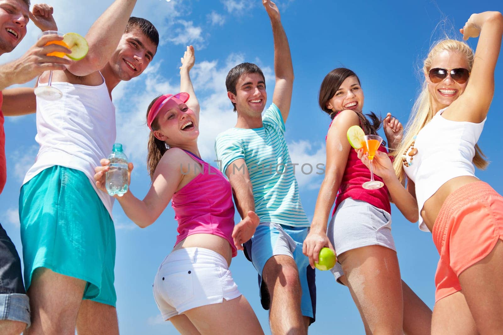 Portrait of happy young friends with cocktails dancing at beach party
