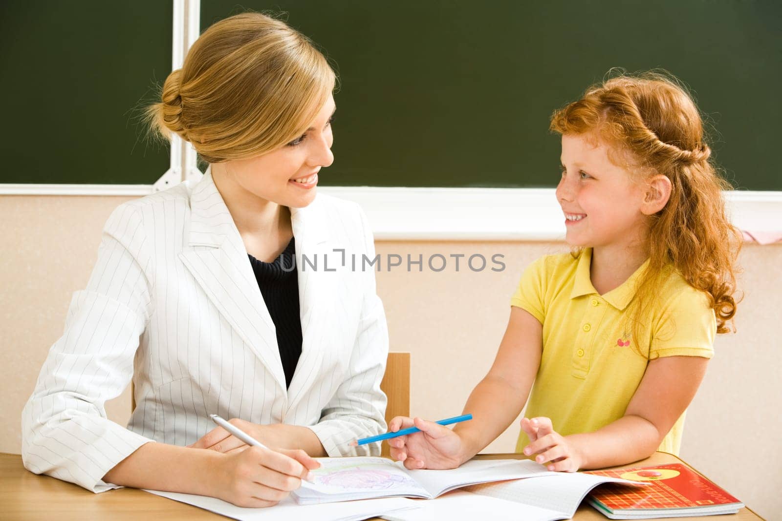 Portrait of teacher and cute schoolgirl sitting at the desk and speaking about lessons
