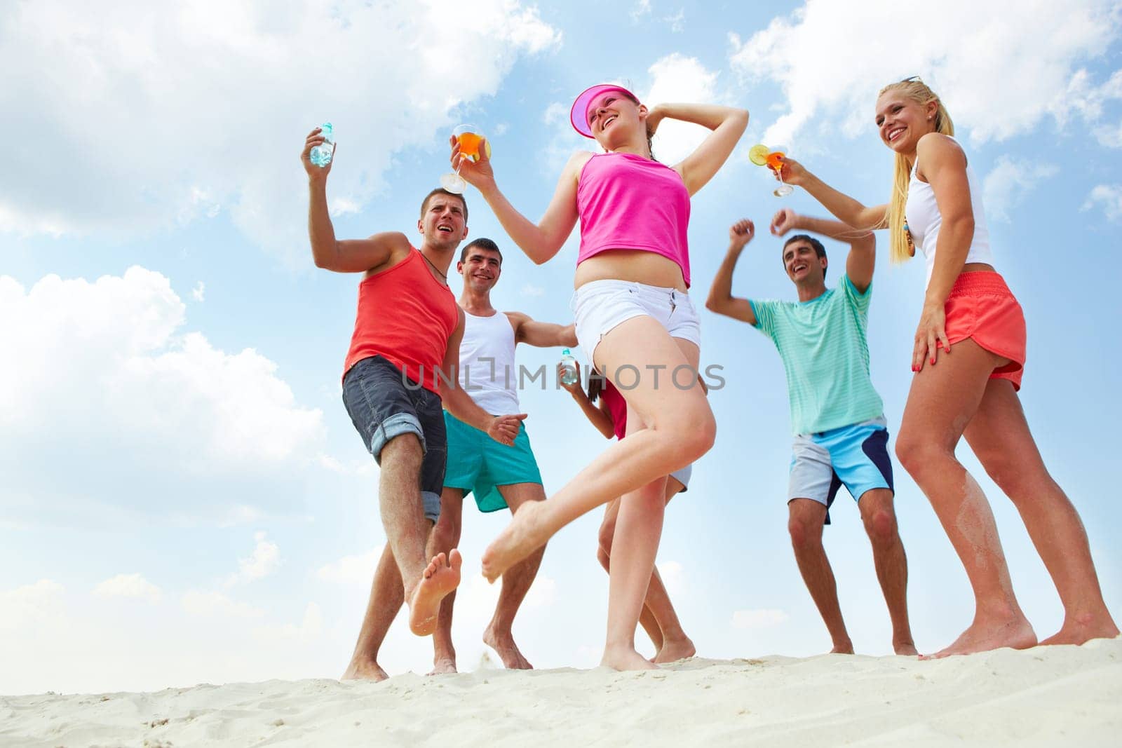 Portrait of happy young friends with cocktails dancing at beach party