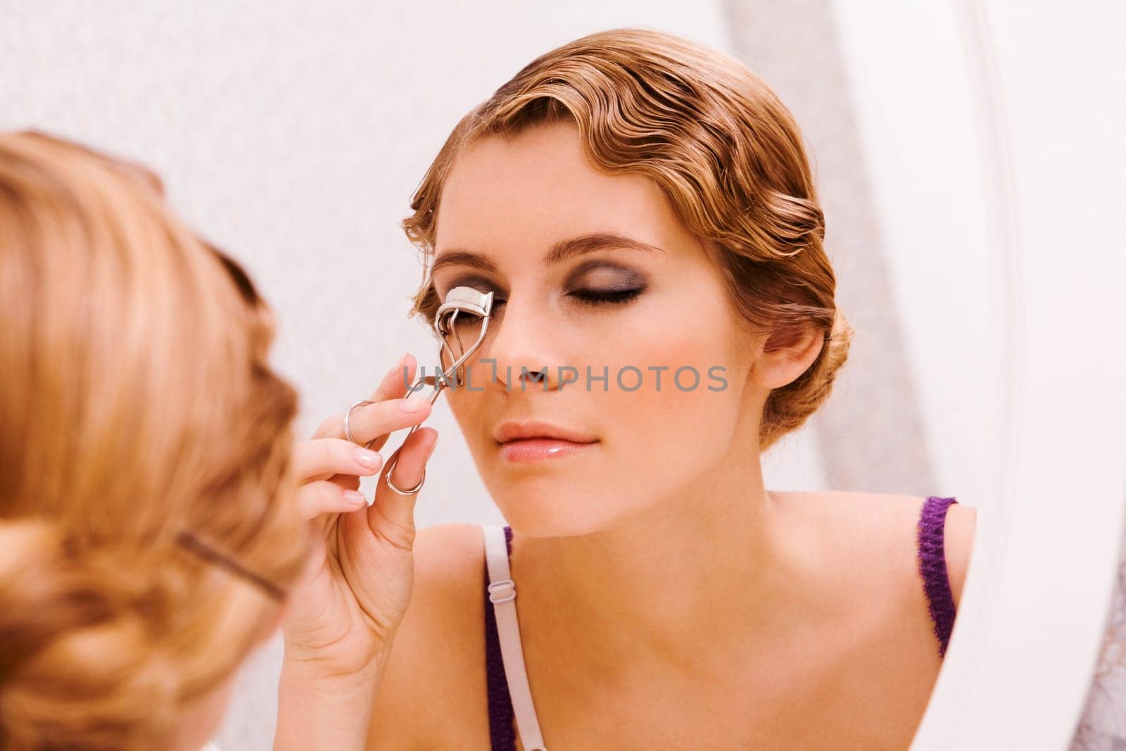 Image of pretty female looking in mirror while curling her eyelashes