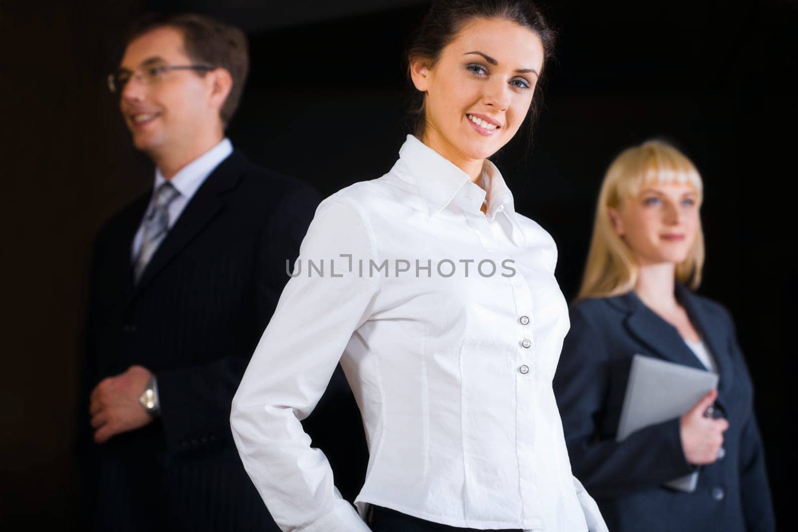 Portrait of three business people on the black background with a beautiful smiling businesswoman at the front
