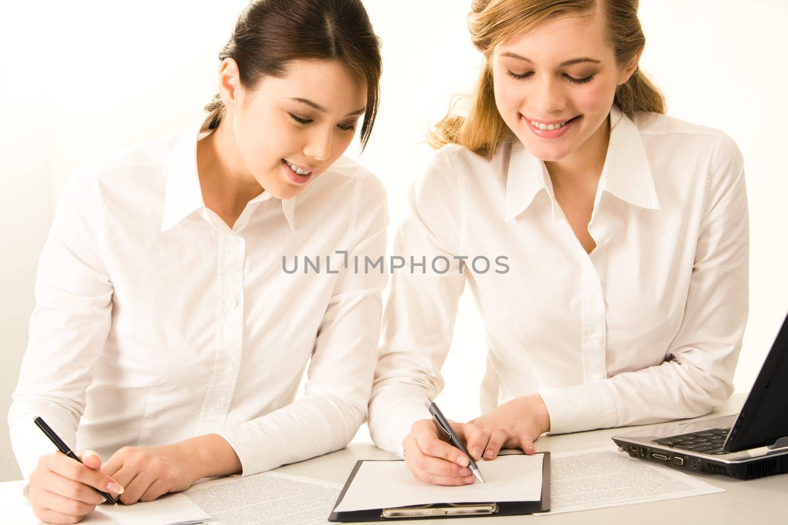 Photo of two business women working with documents and writing something on paper