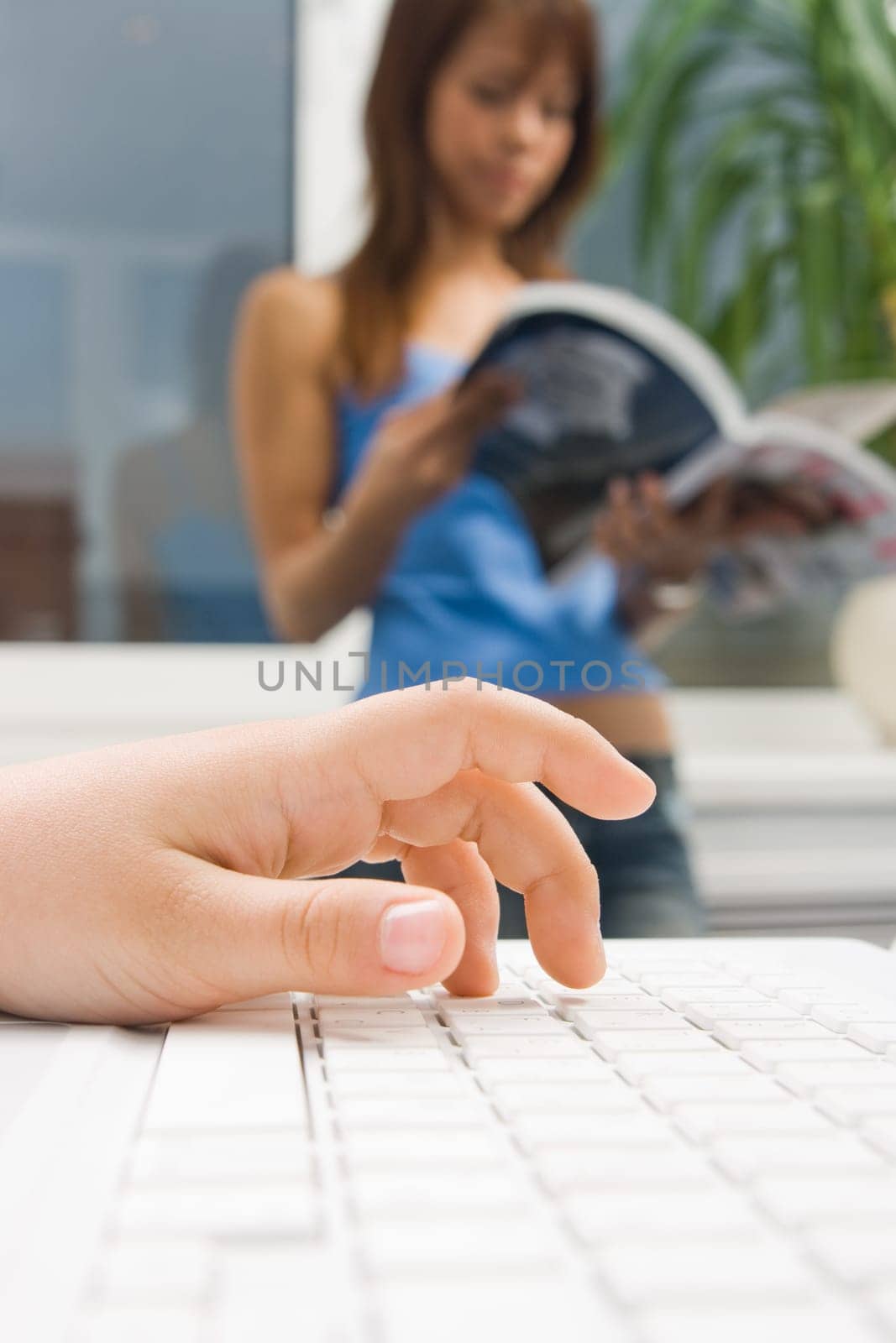 Close-up of childs palm over computer keyboard with female reader at background