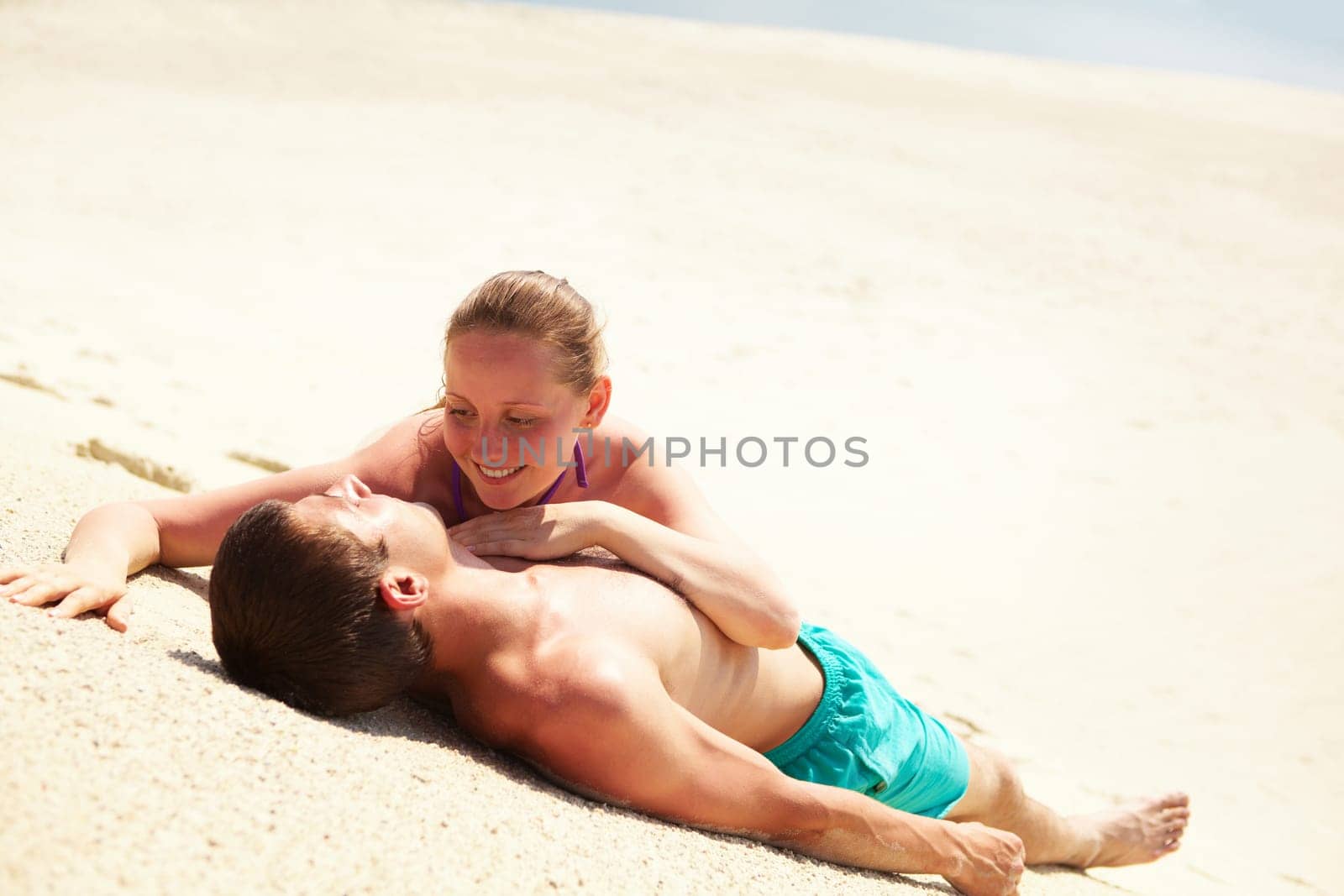 Photo of pretty woman looking at her husband while both lying on sand