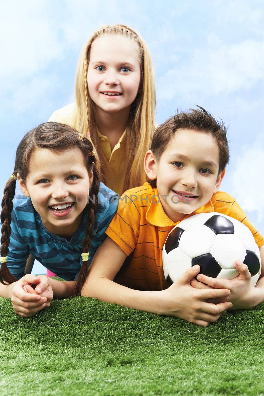 Image of happy friends lying on the grass with ball and looking at camera