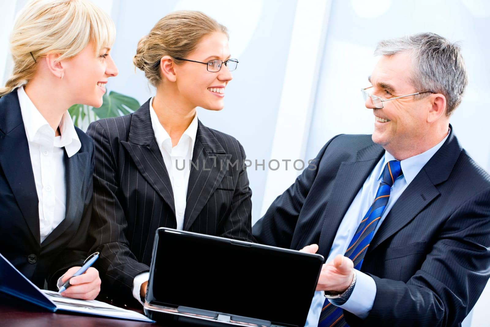 Portrait of three businesspeople sitting near laptop and discussing working ideas in the office