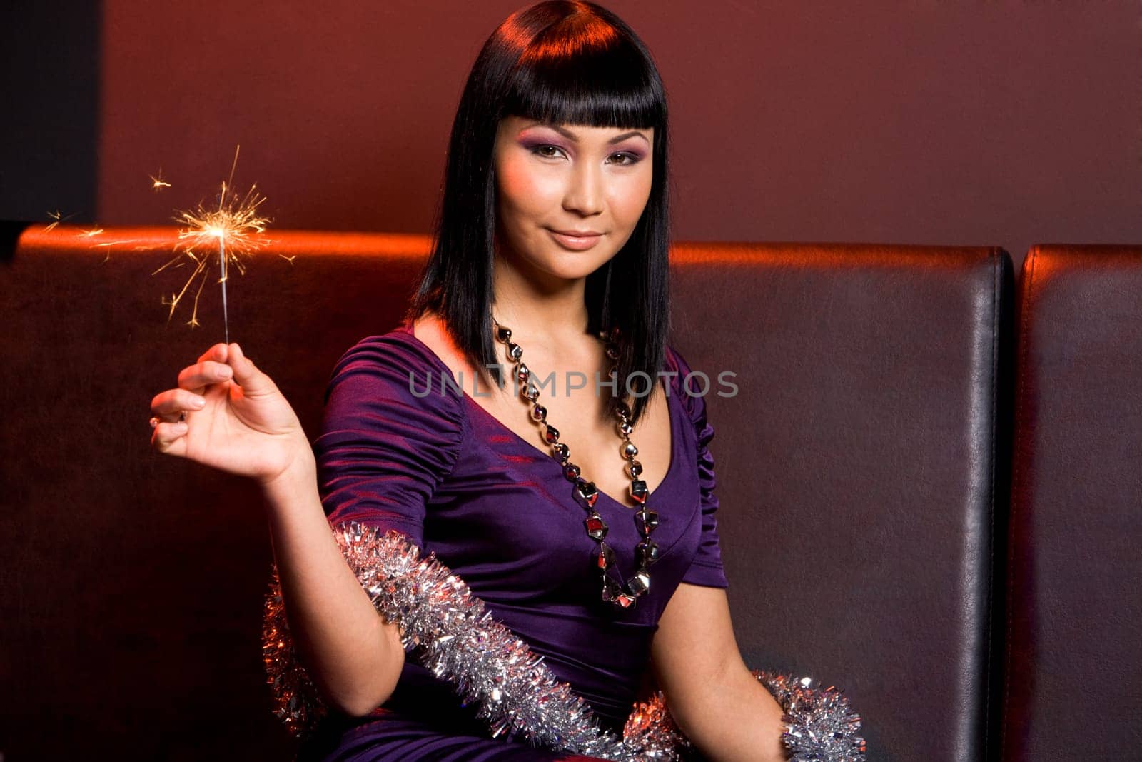 Portrait of charming woman holding sparkler in hand and looking at camera