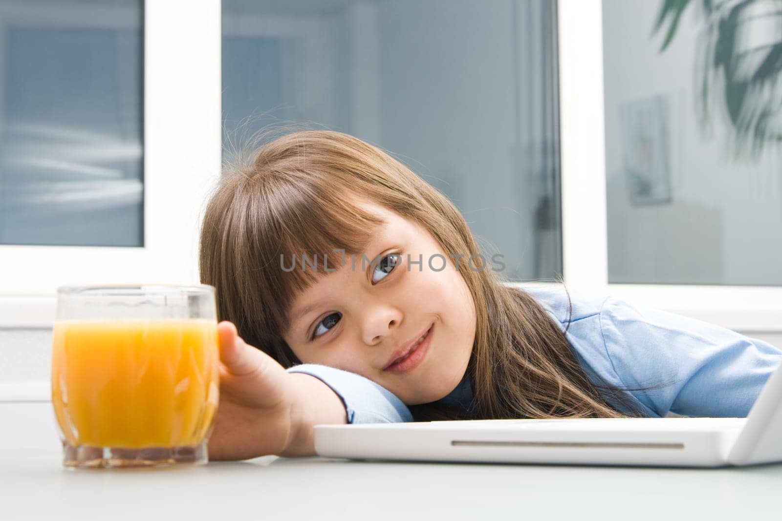 Image of cheerful girl touching a glass of orange juice on table