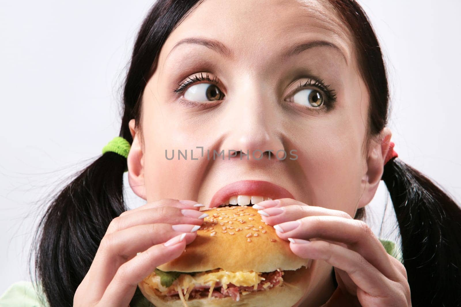 Image of hungry girl eating hamburger and looking aside