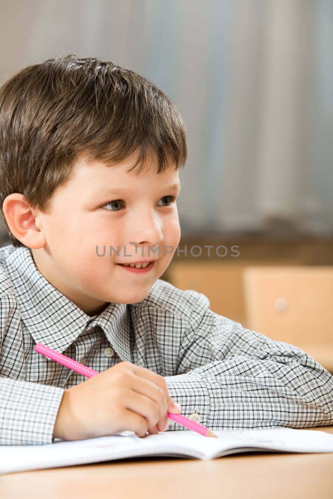 Portrait of smart boy sitting in class and drawing something in copybook while listening to the teacher during lesson