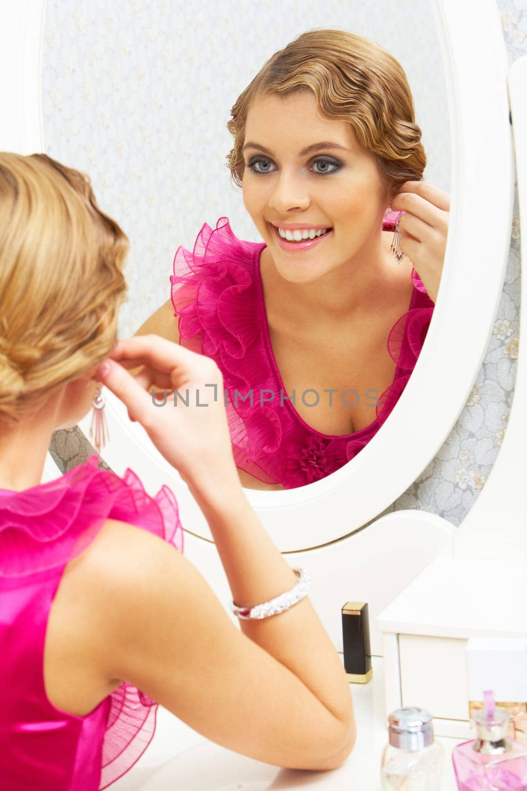 Image of pretty female looking in mirror and putting on earrings