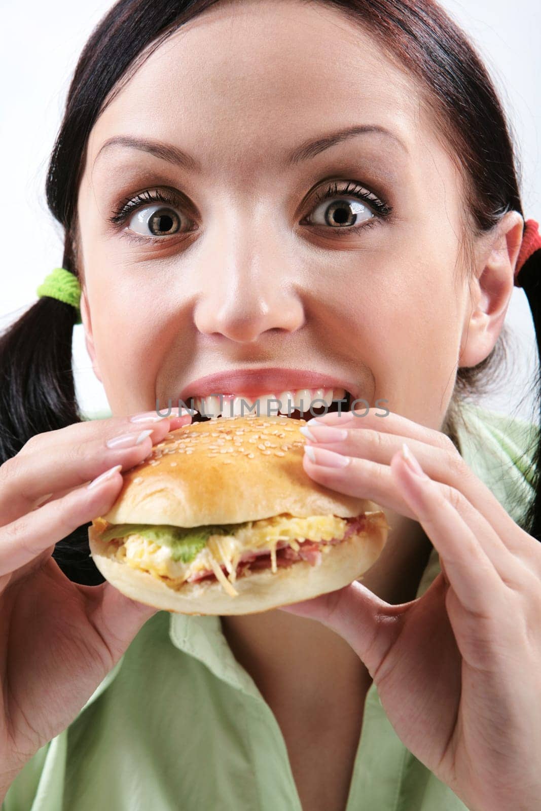 Image of hungry girl eating hamburger and looking at camera