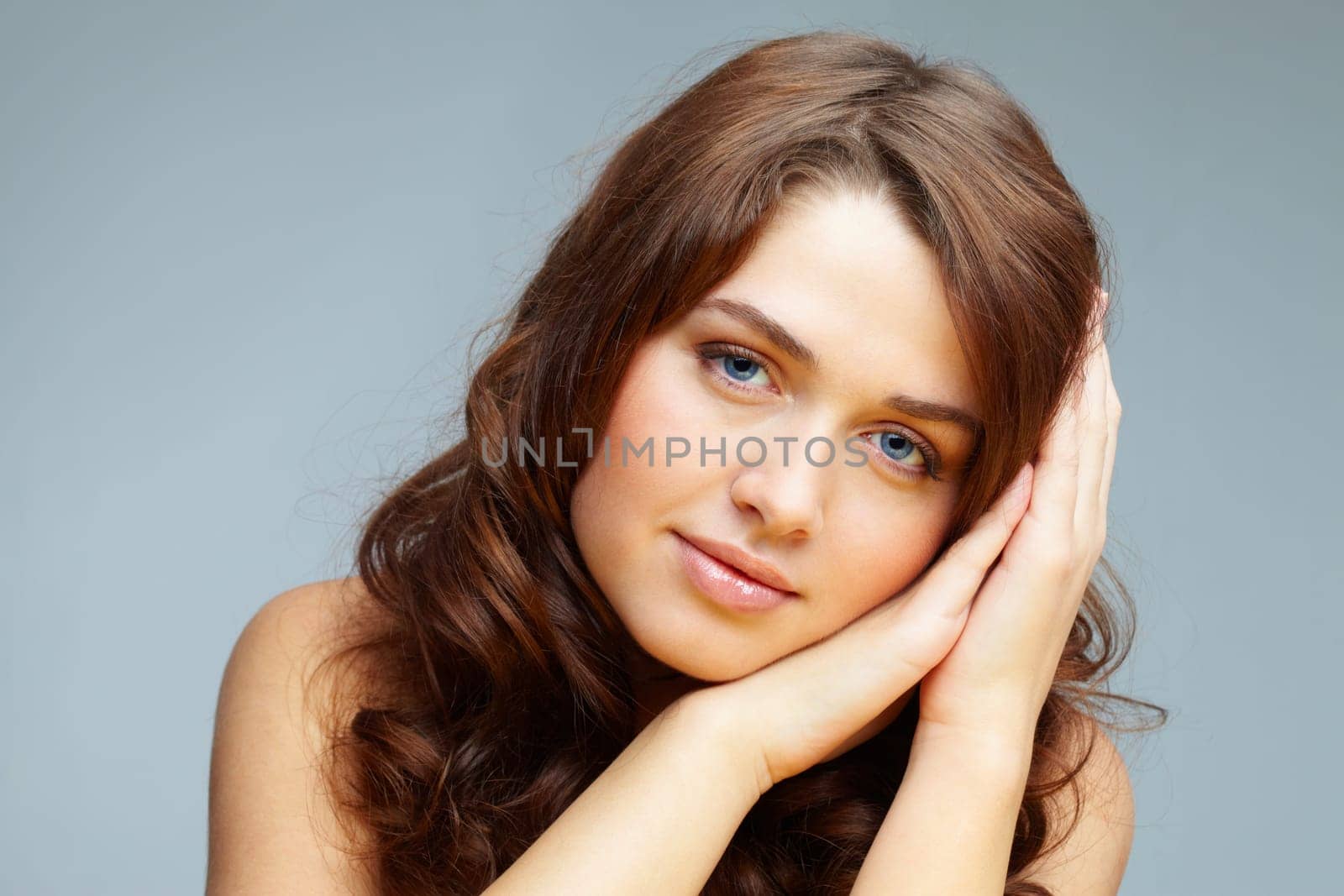Fresh girl with hands by her cheek looking at camera over grey background
