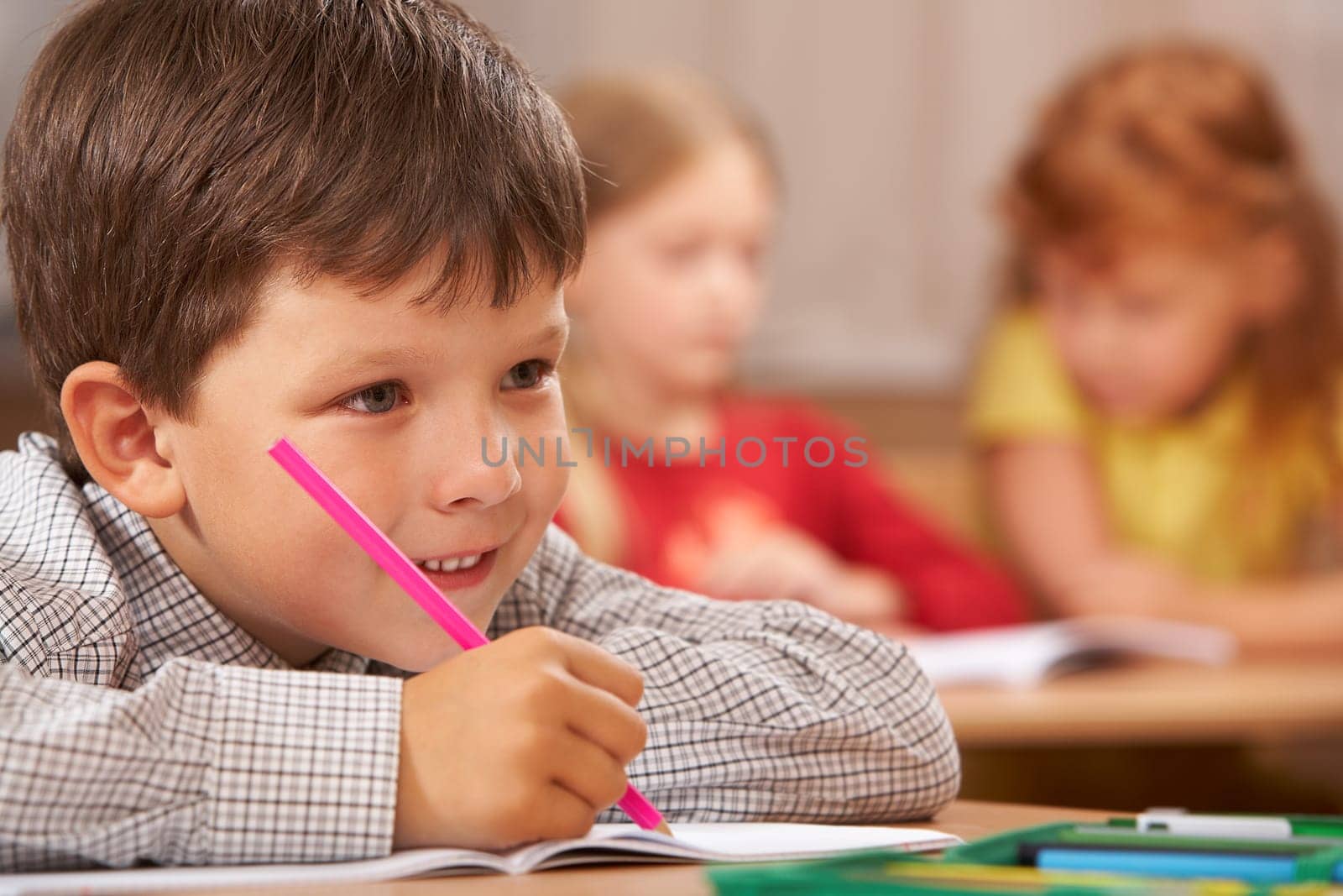 Portrait of smart boy sitting in class and drawing something in copybook while listening to the teacher during lesson