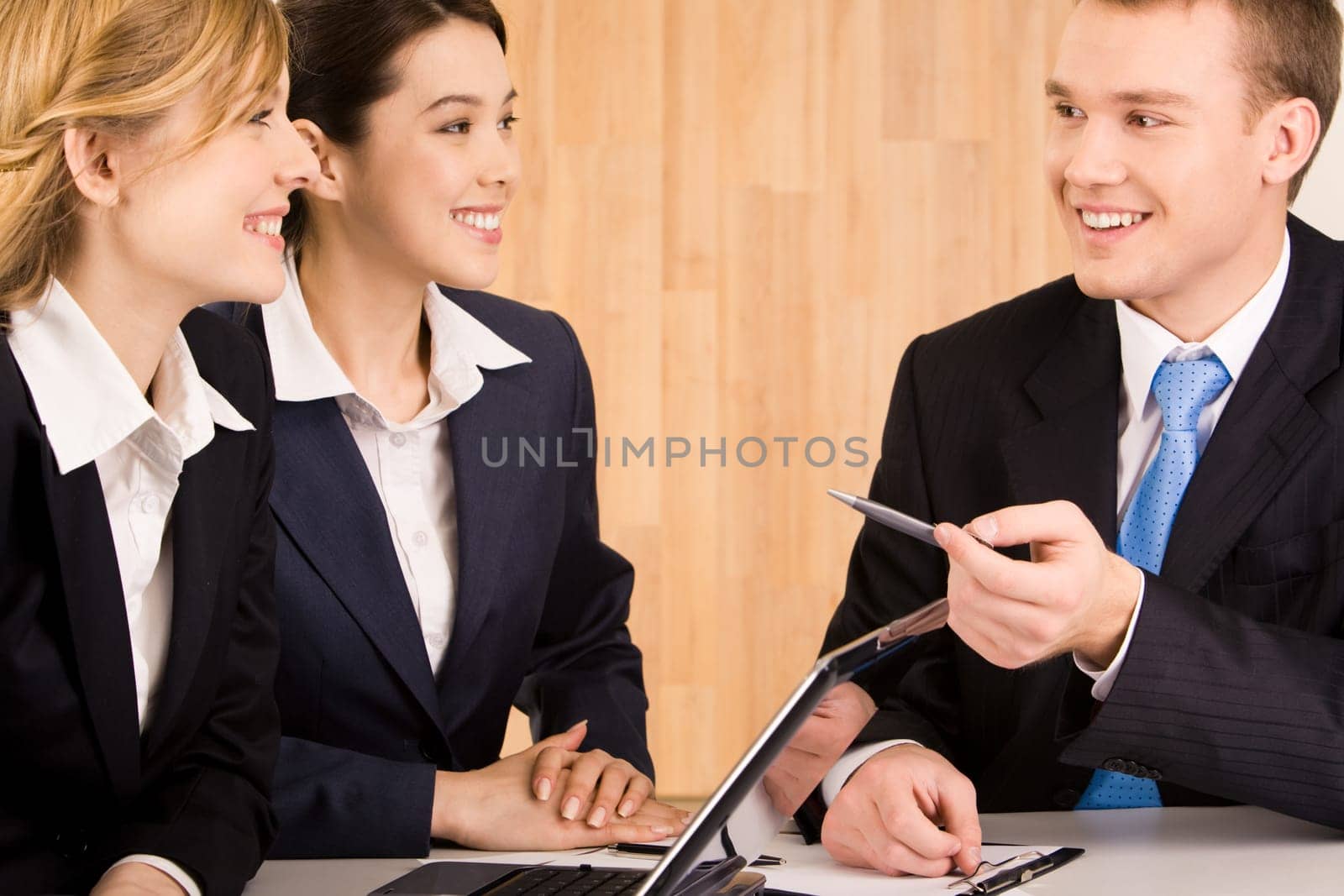 Portrait of happy businessman speaking to his colleagues at meeting while they listening to him with smiles
