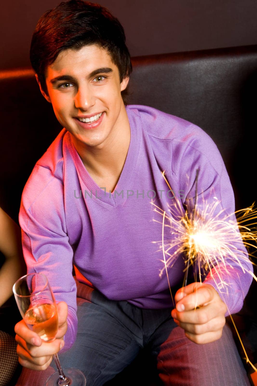 Portrait of joyful guy holding sparkling light and flute with champagne at party