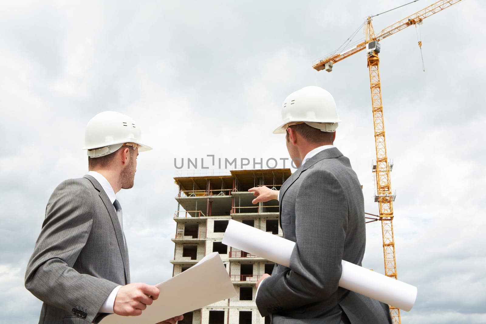 Photo of young engineer showing something to his partner at building site