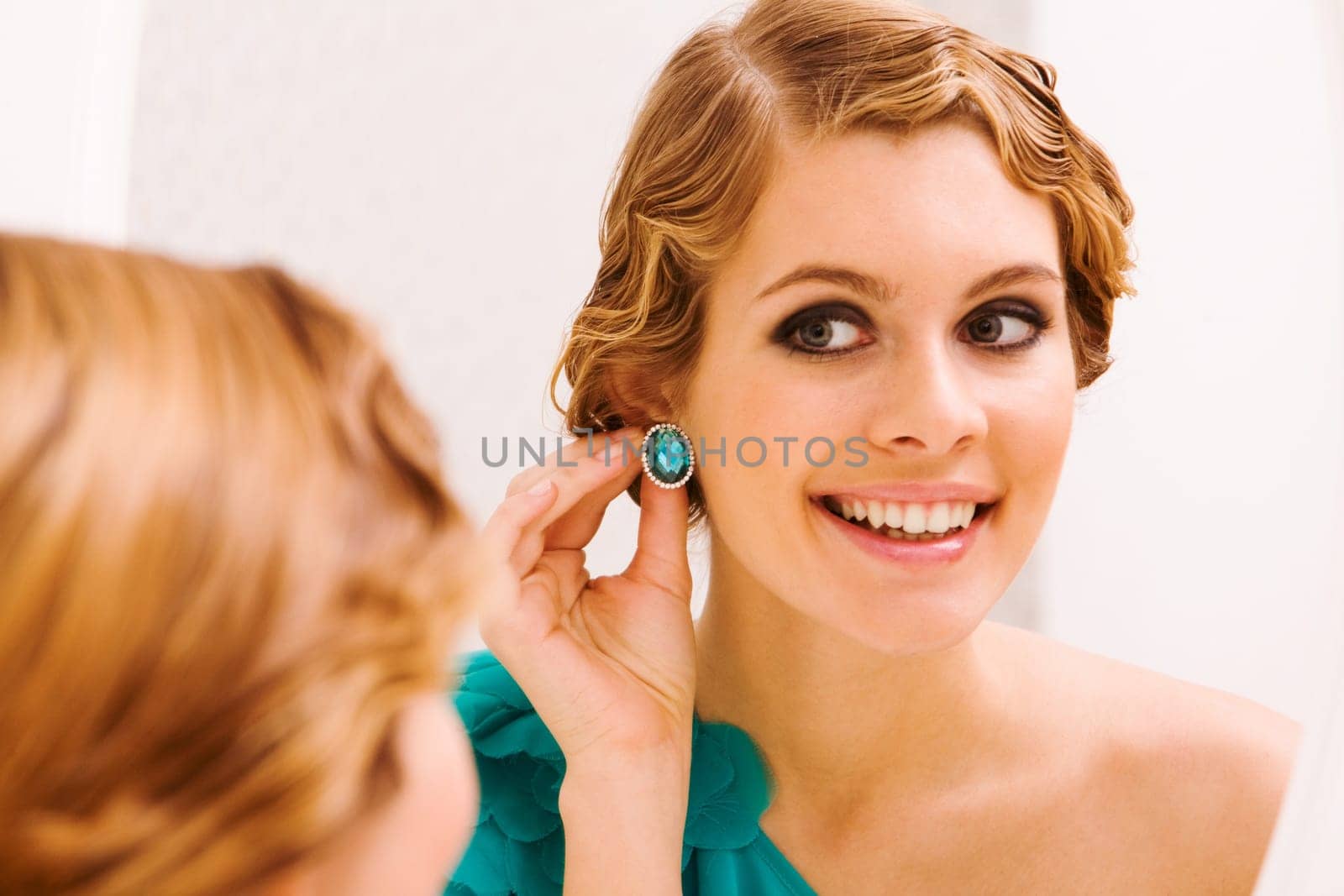Image of pretty female looking in mirror and putting on earrings