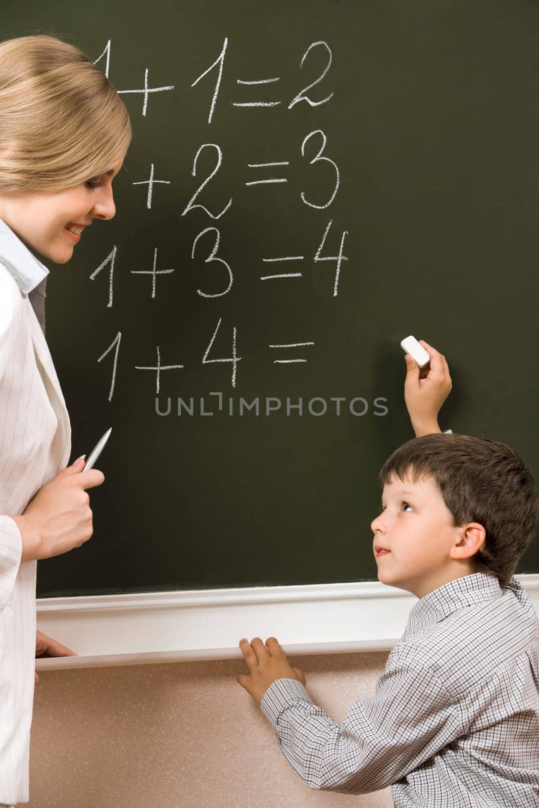 Portrait of diligent pupil looking at his teacher near blackboard while doing sums