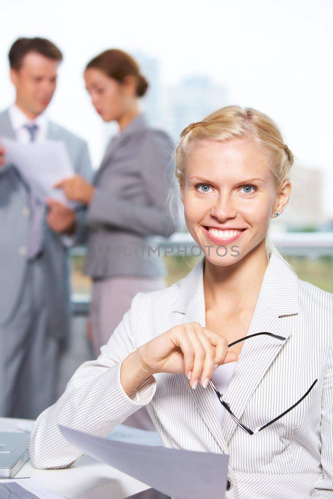 Confident businesswoman looking at camera at background of communicating people