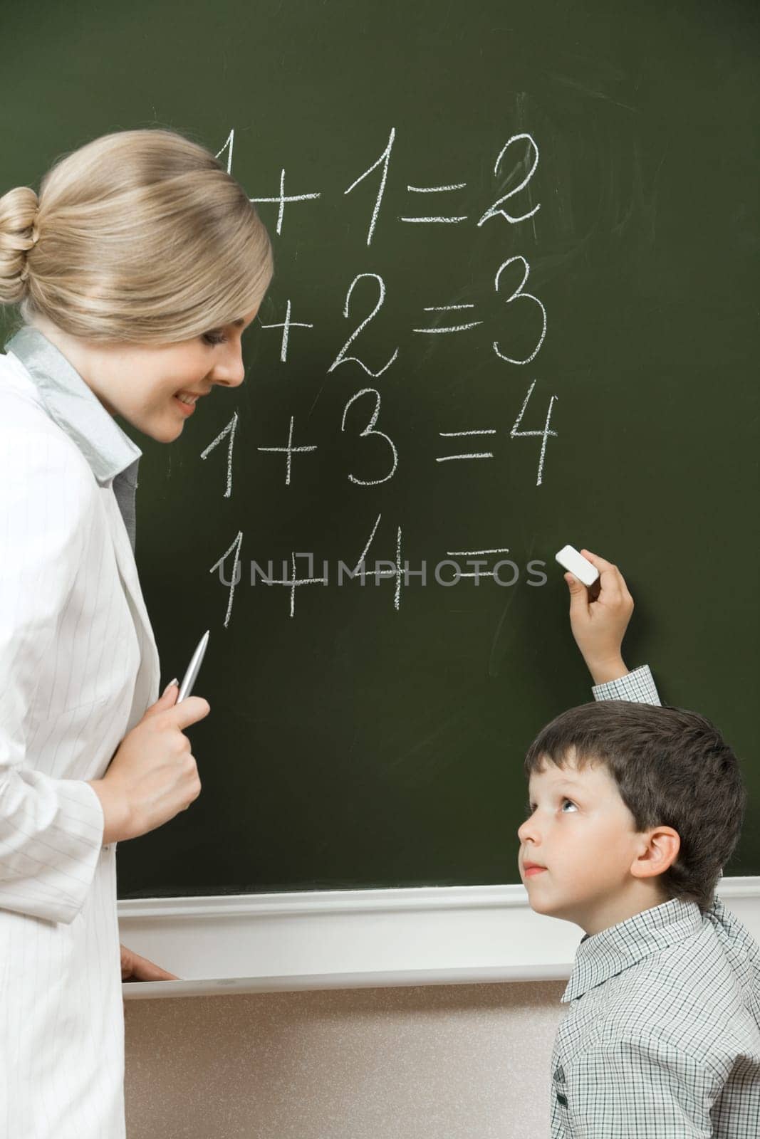 Portrait of diligent pupil looking at his teacher near blackboard while doing sums