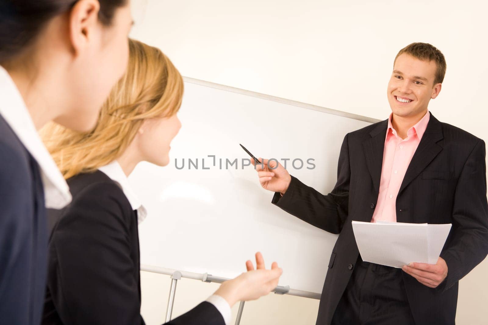 Photo of successful businessman standing at white board while two ladies looking at him during seminar