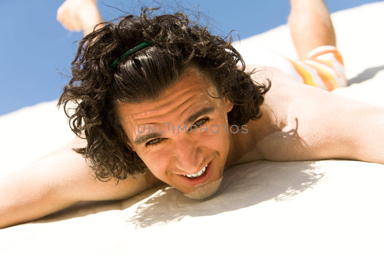 Happy guy lying on sand with outstretched arms and looking at camera on beach