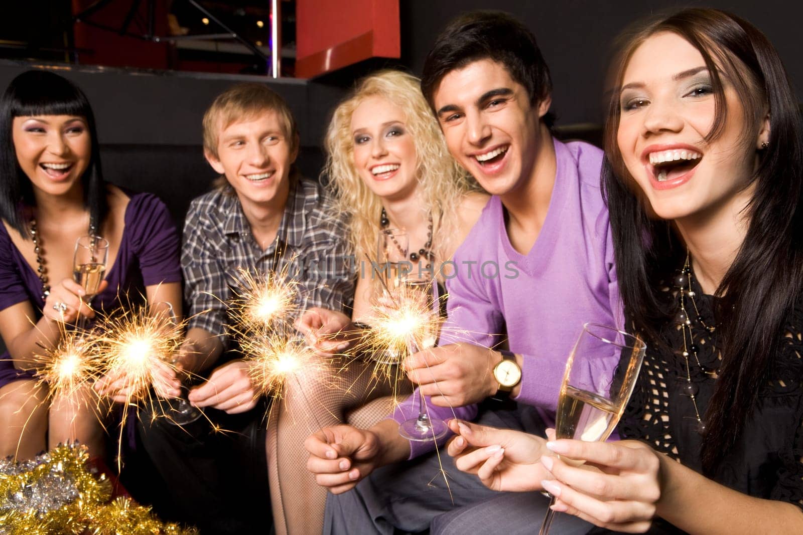 Row of joyful friends with champagne and xmas lights celebrating New Year