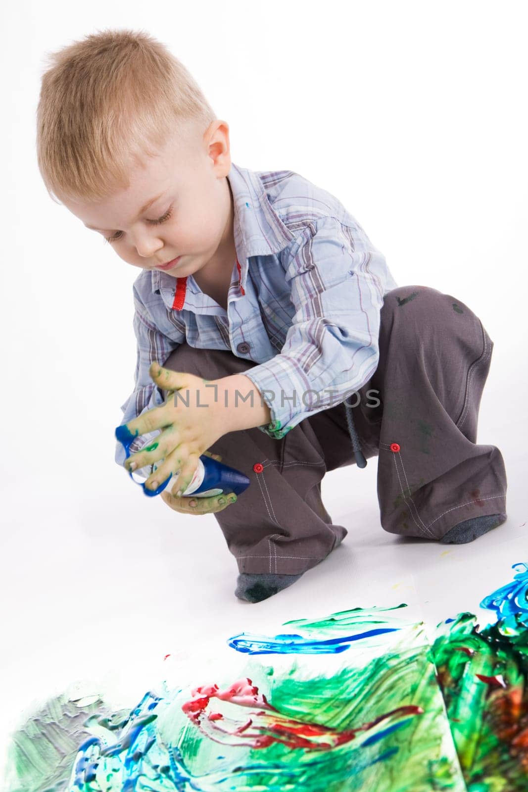 Photo of cute lad holding container with colorful gouache while painting