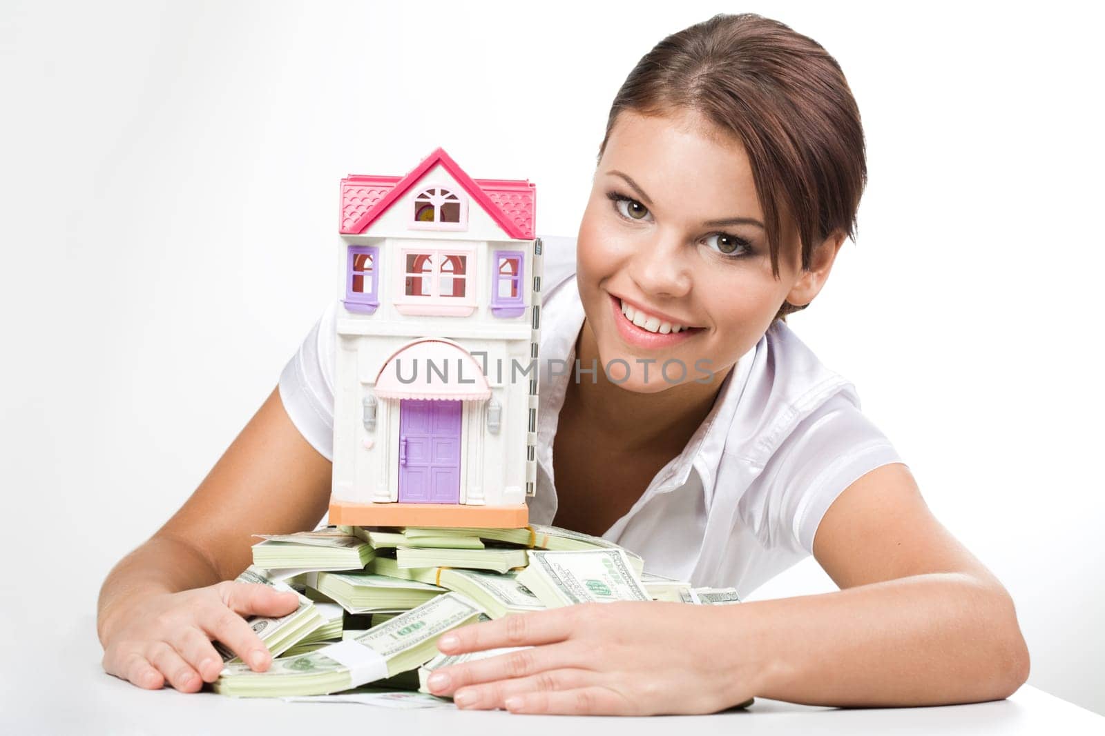 Portrait of lucky woman raking up heap of money with toy house on its top