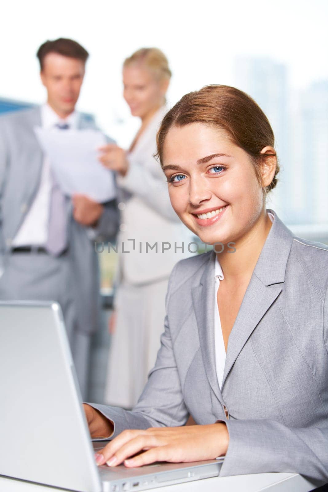 Confident businesswoman looking at camera while typing at background of communicating people