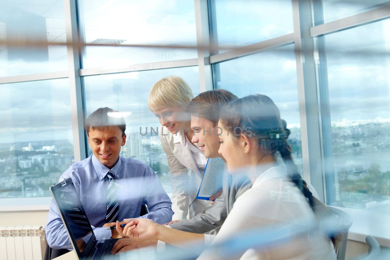 Portrait of several colleagues looking at laptop screen during meeting in office