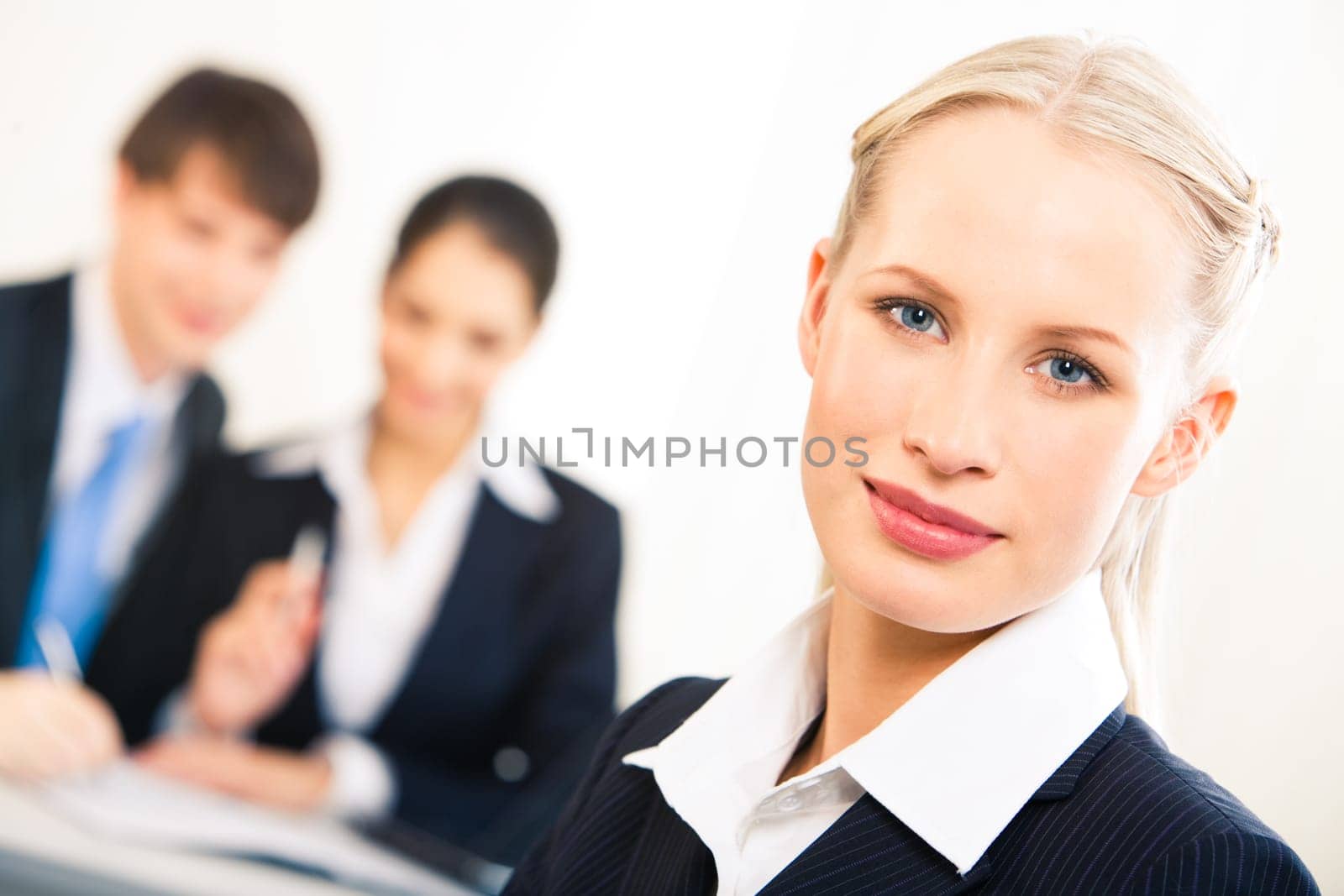 Portrait of blonde businesswoman looking at camera on background of working people
